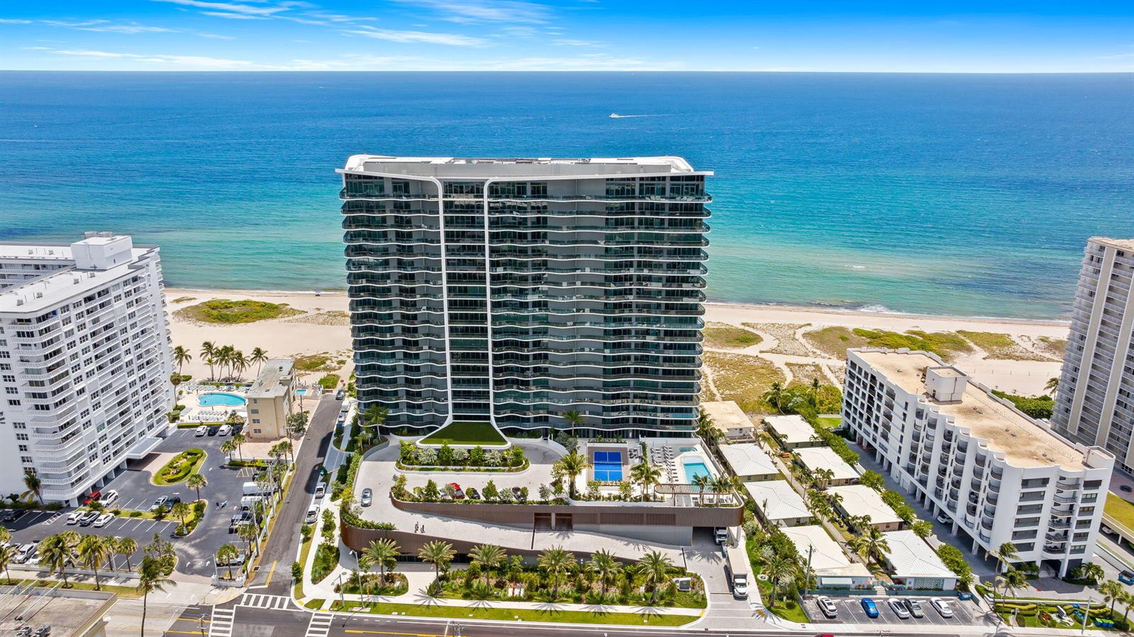 An aerial view shows a modern high-rise condominium building situated directly on a sandy beach — 900 N Ocean Boulevard # 906, Pompano Beach FL 33062, POMPANO BEACH, FL