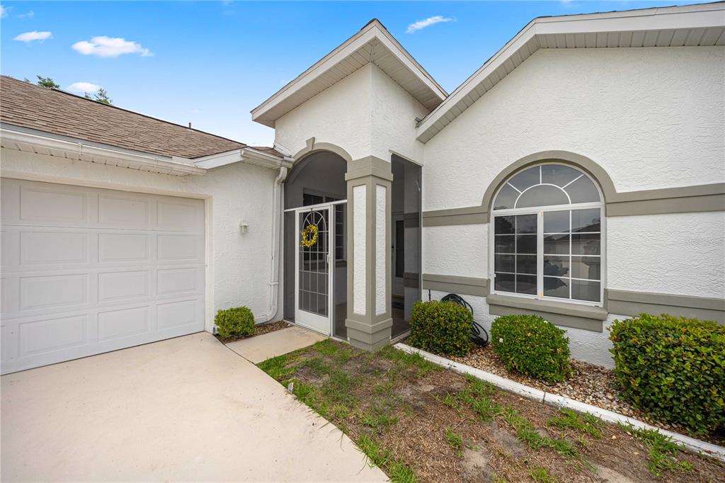 A white stucco house with a garage, arched window, and a screened-in front entryway — 2379 NW 55TH AVENUE ROAD, OCALA, FL