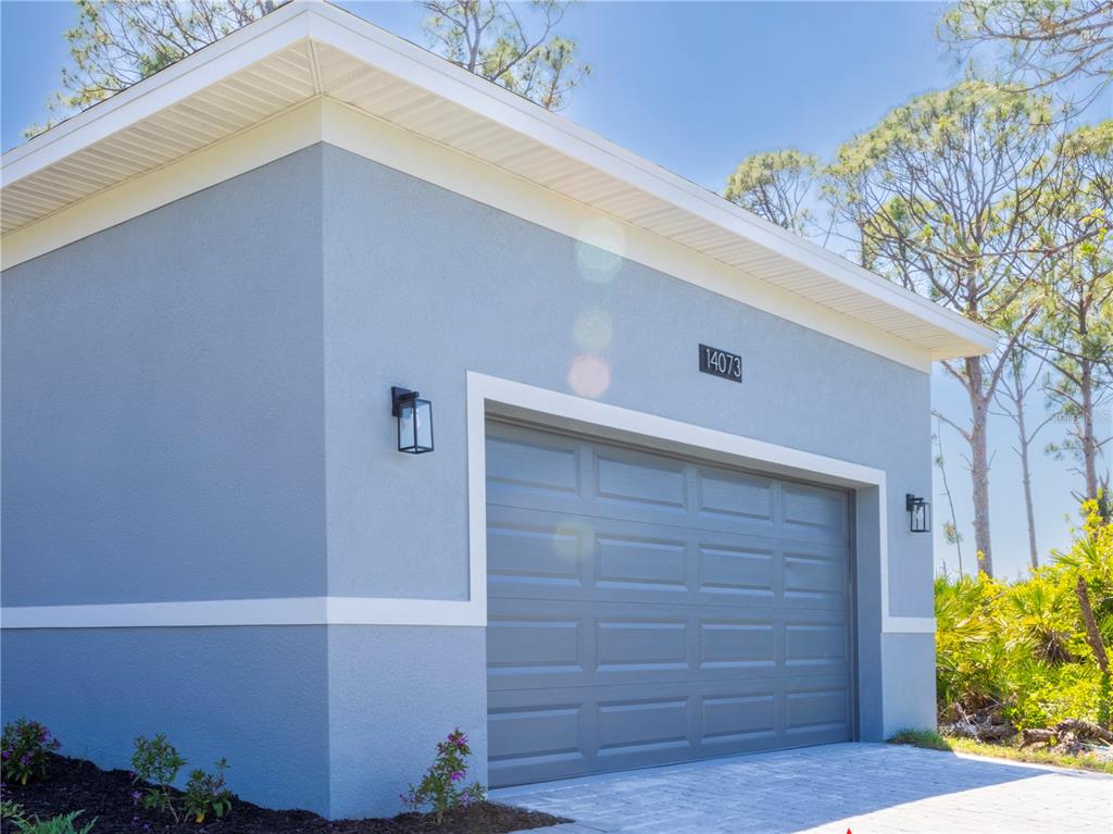 A light blue exterior wall features a gray garage door and two black wall sconces — 9443 HALLENDALE DRIVE, PORT CHARLOTTE, FL