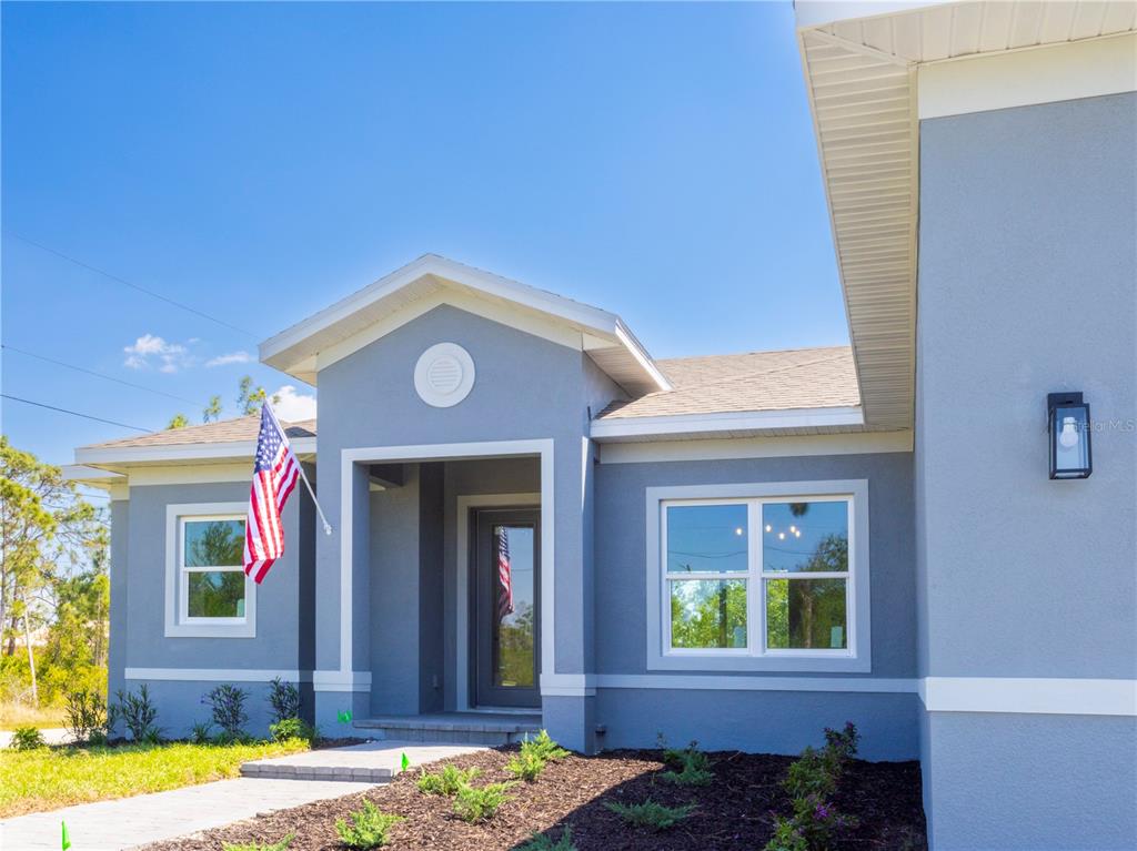 A blue single-story house exterior features a front porch, a flag, and a landscaped yard — 9443 HALLENDALE DRIVE, PORT CHARLOTTE, FL