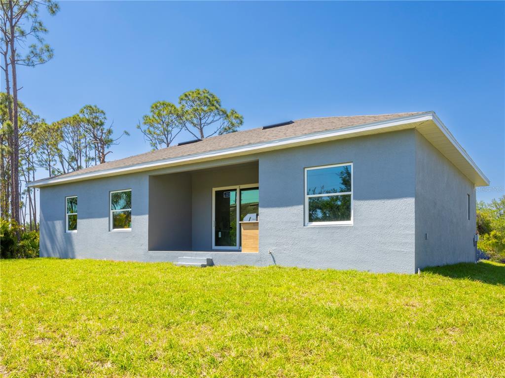 The rear exterior of a gray, single-story house features a covered patio and sliding doors — 9443 HALLENDALE DRIVE, PORT CHARLOTTE, FL
