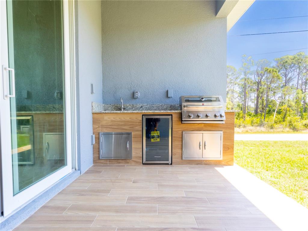 An outdoor kitchen features a built-in grill, beverage cooler, sink, and wood-look tile flooring — 9443 HALLENDALE DRIVE, PORT CHARLOTTE, FL