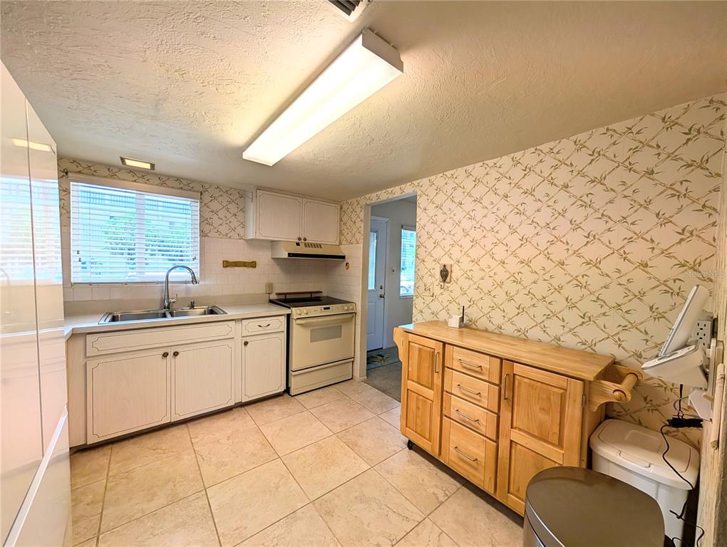 A kitchen features white cabinets, a light-colored tile floor, and patterned wallpaper — 2303 SUNSET DRIVE UNIT H7, BRADENTON, FL