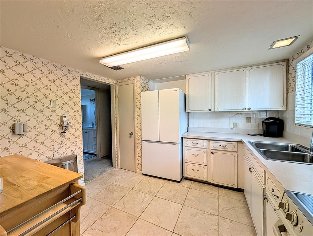 A kitchen features white cabinets, a white refrigerator, tiled floors, and patterned wallpaper — 2303 SUNSET DRIVE UNIT H7, BRADENTON, FL