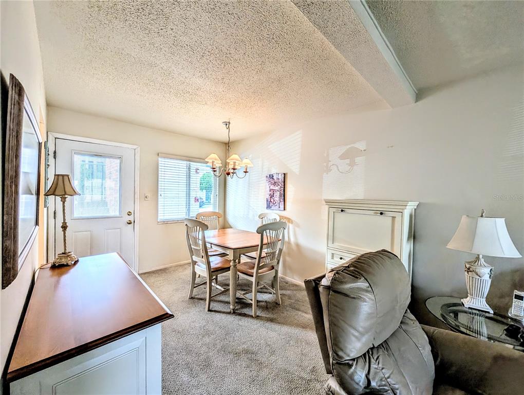 A dining area with carpeted floors, a wooden table, four chairs, and a chandelier — 2303 SUNSET DRIVE UNIT H7, BRADENTON, FL