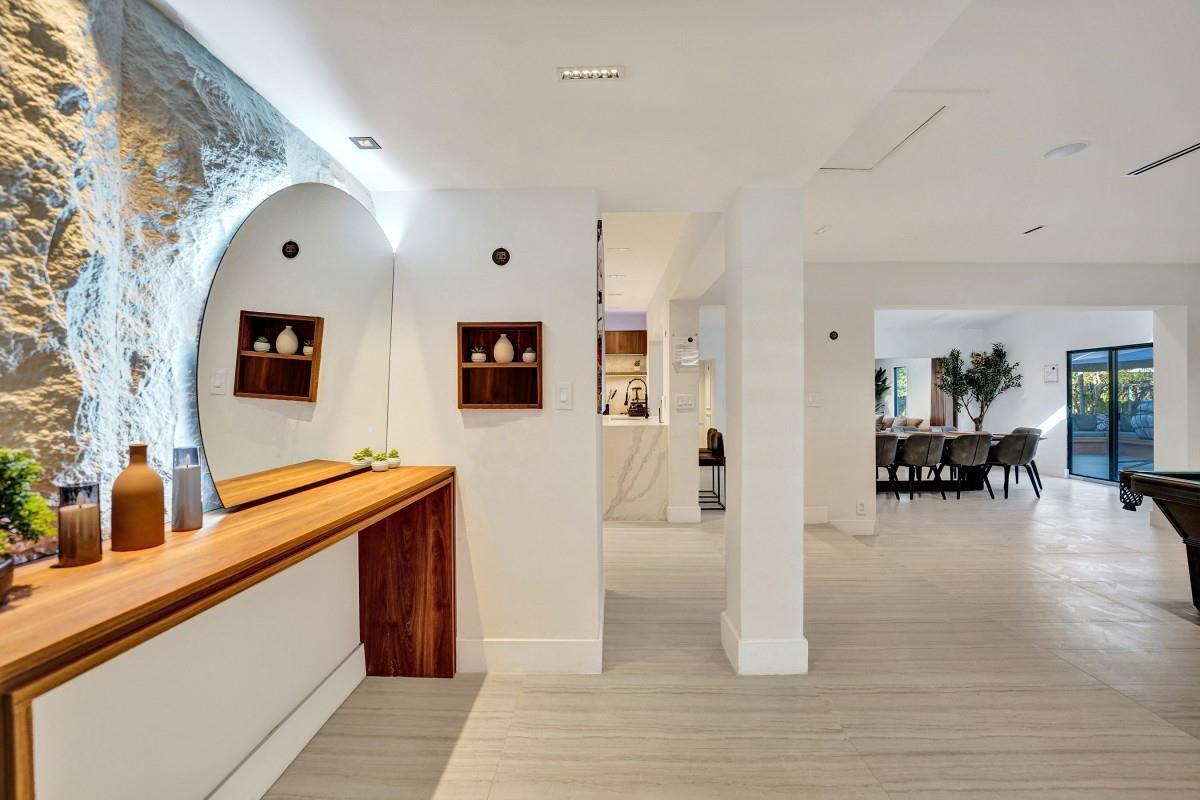 A modern interior featuring a stone accent wall, a large circular mirror, and wood cabinetry — 4417 SW 38th Terrace, Dania Beach FL 33312, DANIA BEACH, FL