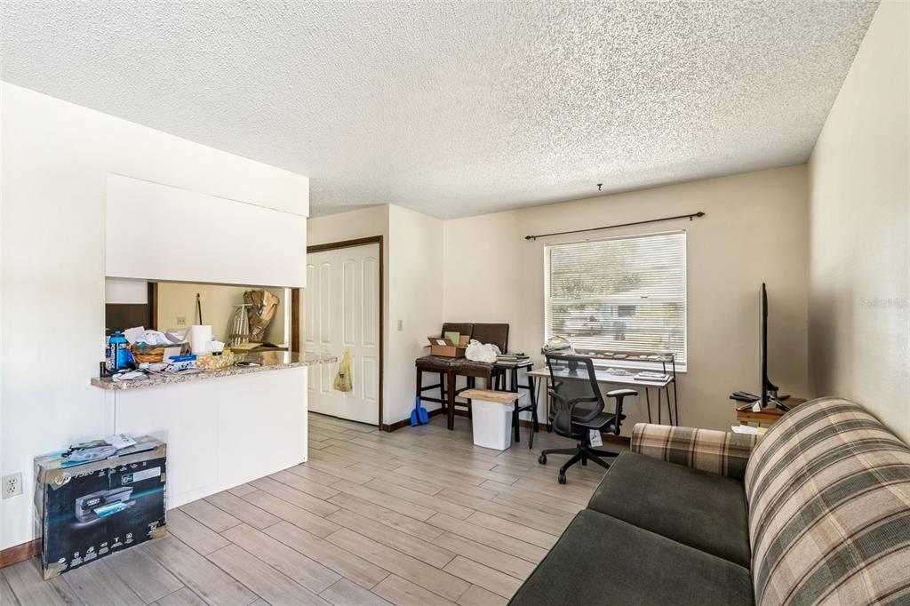 A living room with light tile flooring, a plaid sofa, a desk, and a kitchen pass-through — 6404 S ADELIA AVENUE, TAMPA, FL
