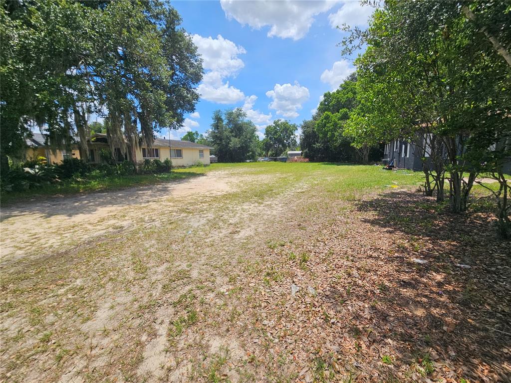 A vacant, grassy lot sits between two houses under a bright, partly cloudy sky — 0 DELMAR STREET, DADE CITY, FL