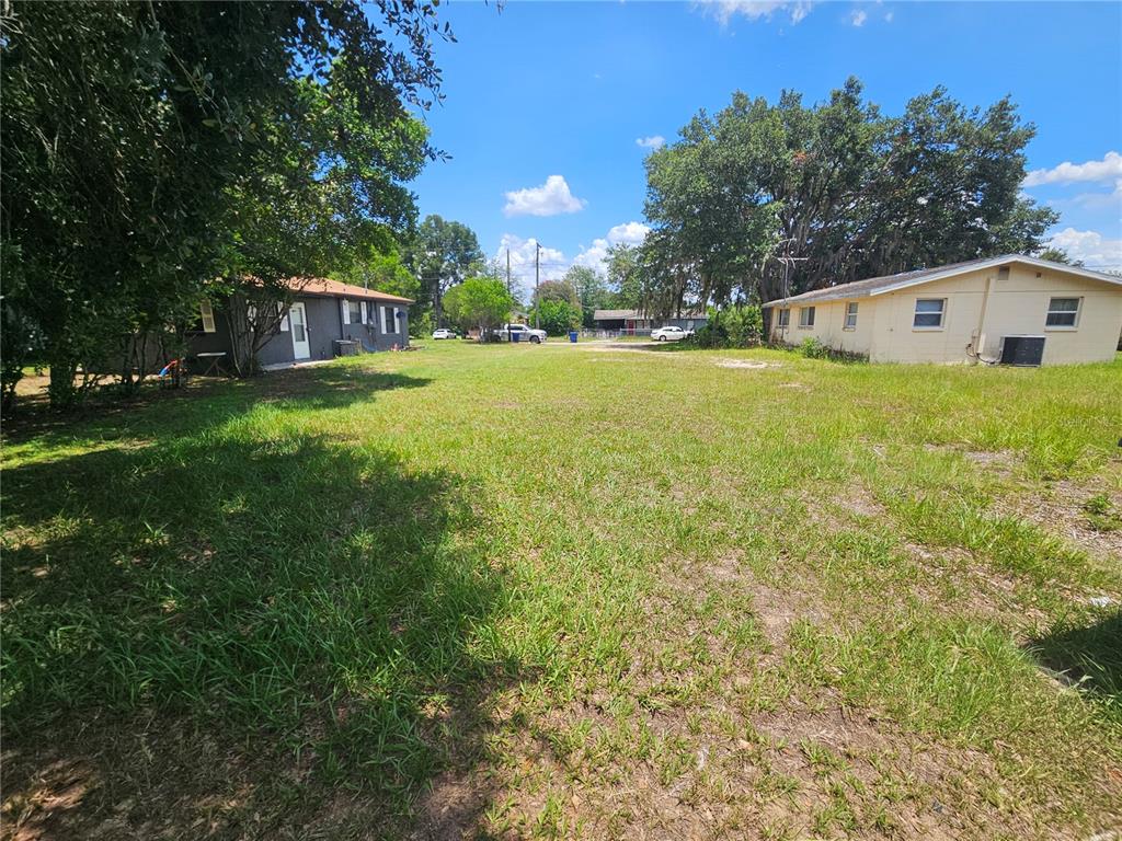 A grassy vacant lot sits between two single-story houses under a clear blue sky — 0 DELMAR STREET, DADE CITY, FL