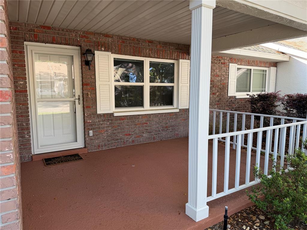 A covered brick porch features a white front door, windows with shutters, and white railings — 9529 SW 85TH AVENUE UNIT D, OCALA, FL