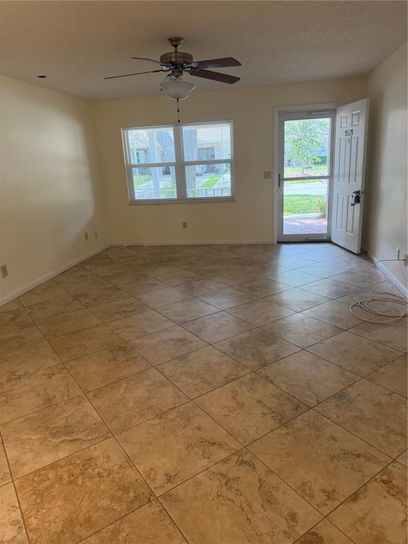 An empty living room features beige tile flooring, a ceiling fan, and an open front door — 9529 SW 85TH AVENUE UNIT D, OCALA, FL