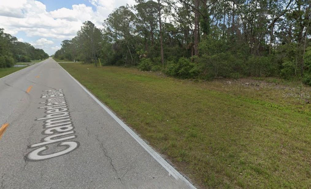 A paved road runs alongside a grassy shoulder and a dense wooded area — 13479 CHAMBERLAIN BOULEVARD, PORT CHARLOTTE, FL