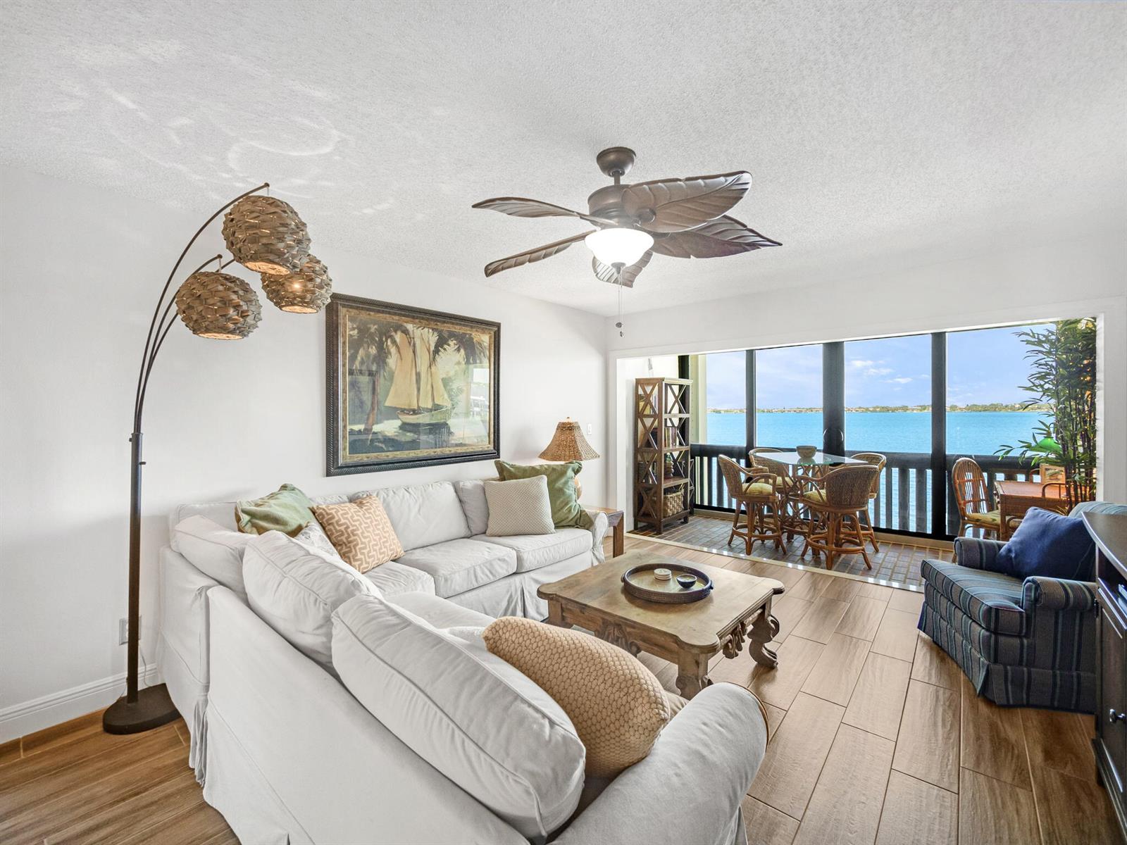 A living room with a white sectional sofa, wood-look tile floors, and a balcony overlooking water — 175 SE Saint Lucie Boulevard # F116, Stuart FL 34996, STUART, FL