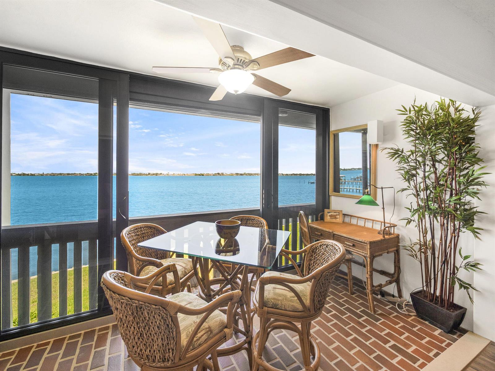 A sunroom features a glass-topped dining set, wicker chairs, a desk, and water views — 175 SE Saint Lucie Boulevard # F116, Stuart FL 34996, STUART, FL