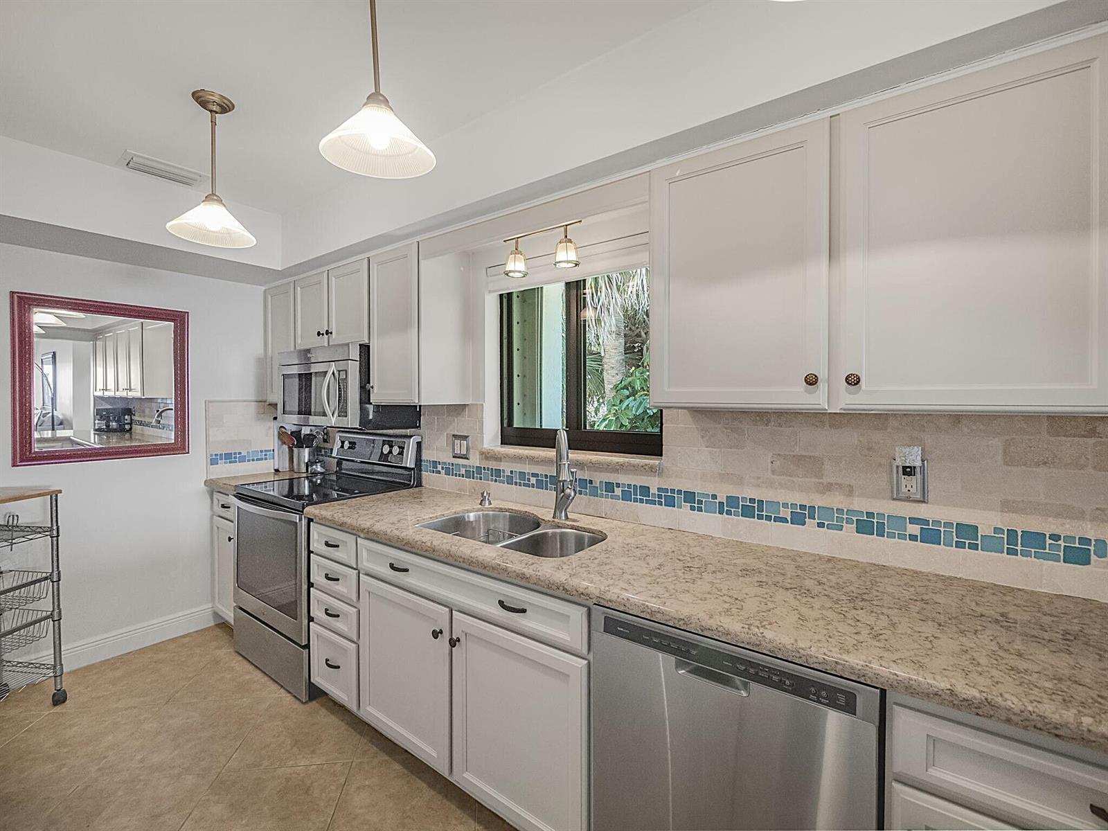 A kitchen features white cabinets, granite countertops, stainless steel appliances, and a blue tiled backsplash — 175 SE Saint Lucie Boulevard # F116, Stuart FL 34996, STUART, FL