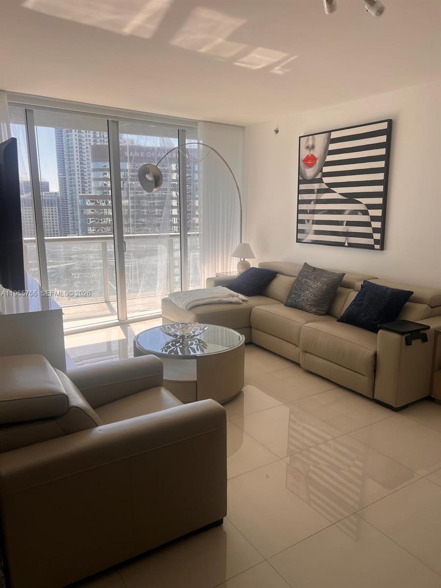 A modern living room features a beige sectional sofa, glass coffee table, and abstract wall art — 475 Brickell Ave # 3613, Miami FL 33131, MIAMI, FL