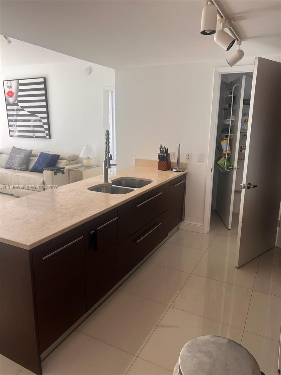 A kitchen island with a sink and dark cabinets sits in front of a pantry — 475 Brickell Ave # 3613, Miami FL 33131, MIAMI, FL