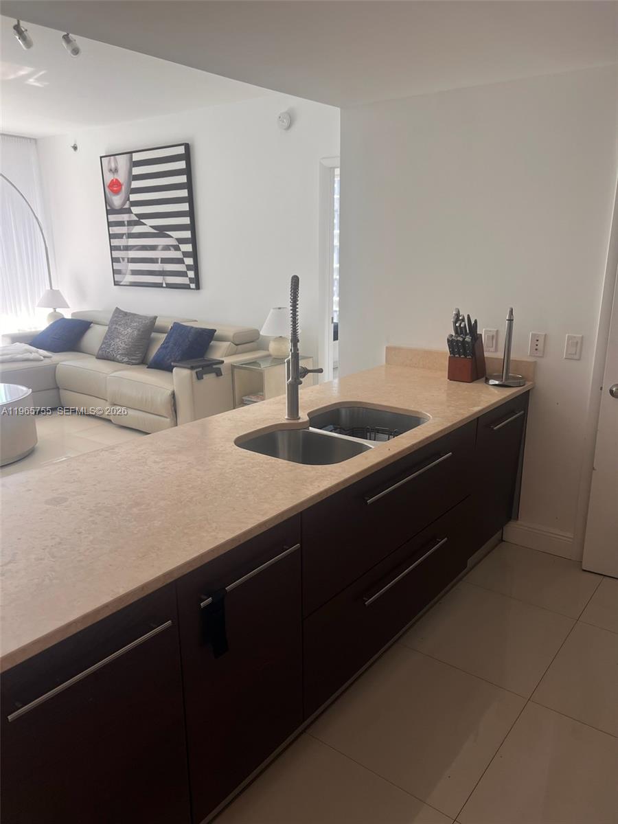 A kitchen island with a double sink and dark cabinets overlooks a living room area — 475 Brickell Ave # 3613, Miami FL 33131, MIAMI, FL