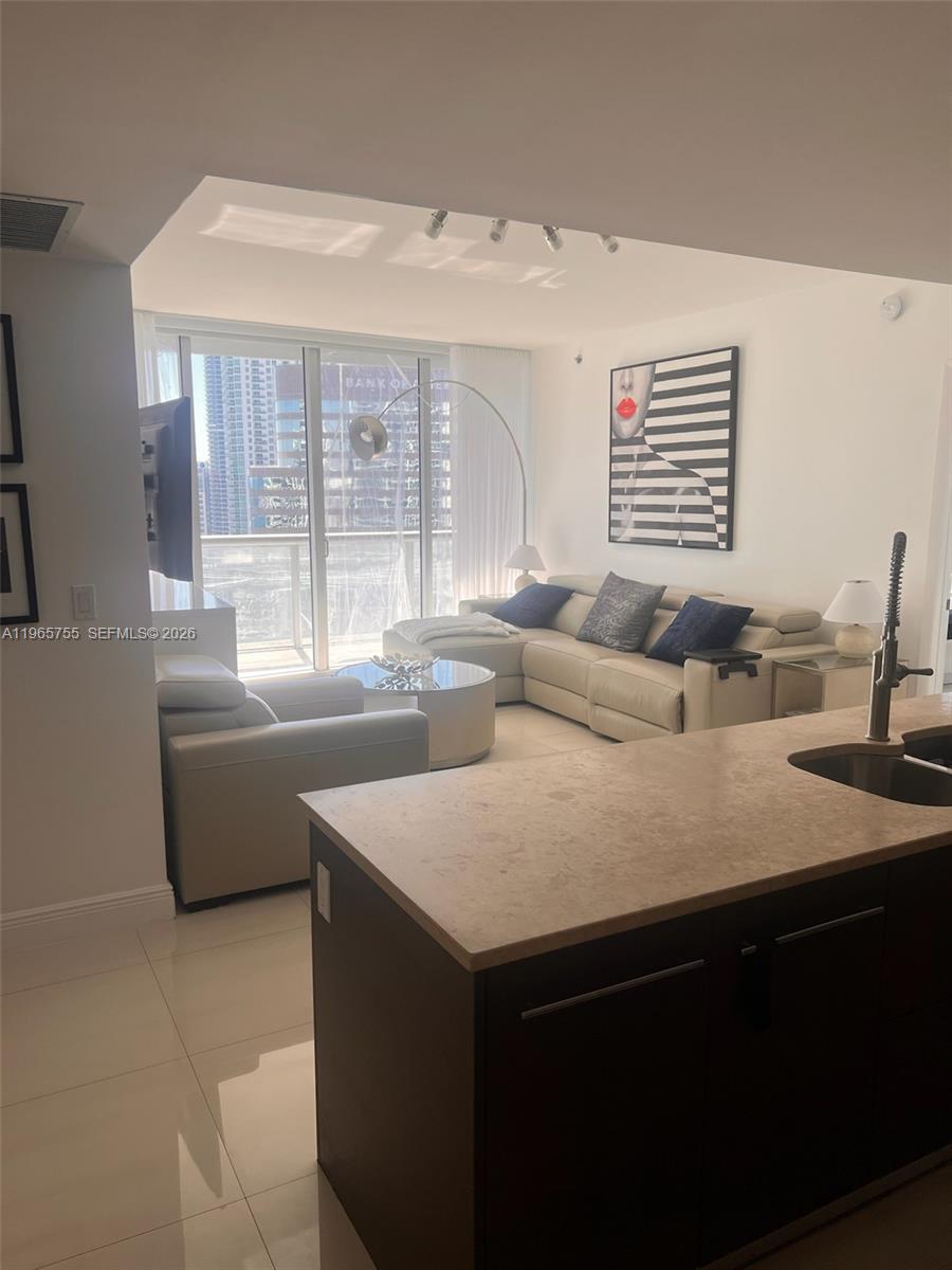 A modern living room with a sectional sofa and kitchen island overlooks a city skyline — 475 Brickell Ave # 3613, Miami FL 33131, MIAMI, FL
