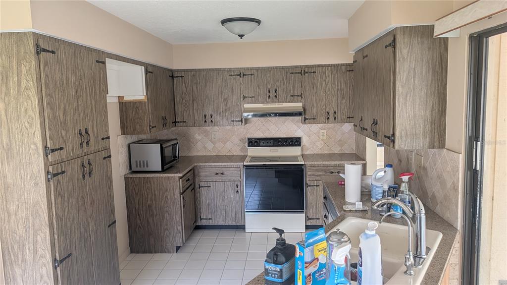 A kitchen features wood-grain cabinets, a white stove, a microwave, and a tiled backsplash — 3720 PIN OAKS STREET, SARASOTA, FL