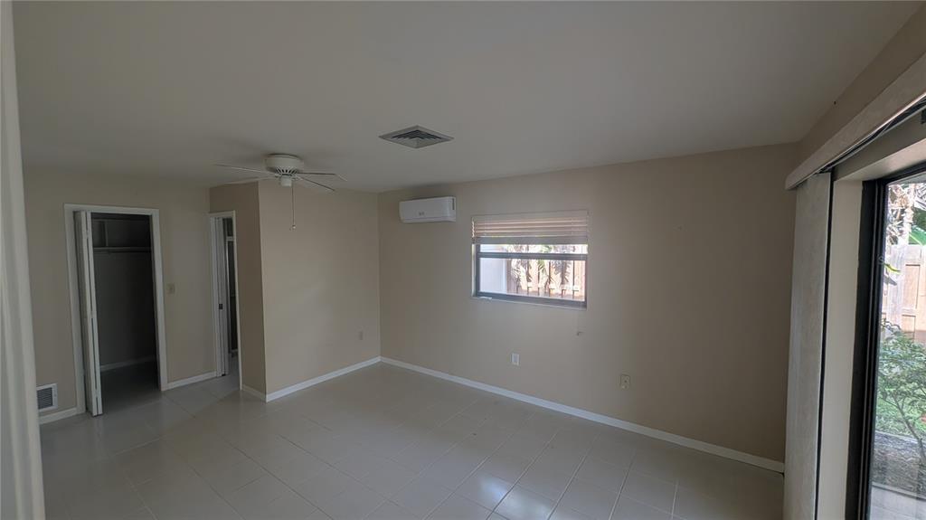 An empty room with beige walls, tile flooring, a ceiling fan, and a wall-mounted AC — 3720 PIN OAKS STREET, SARASOTA, FL
