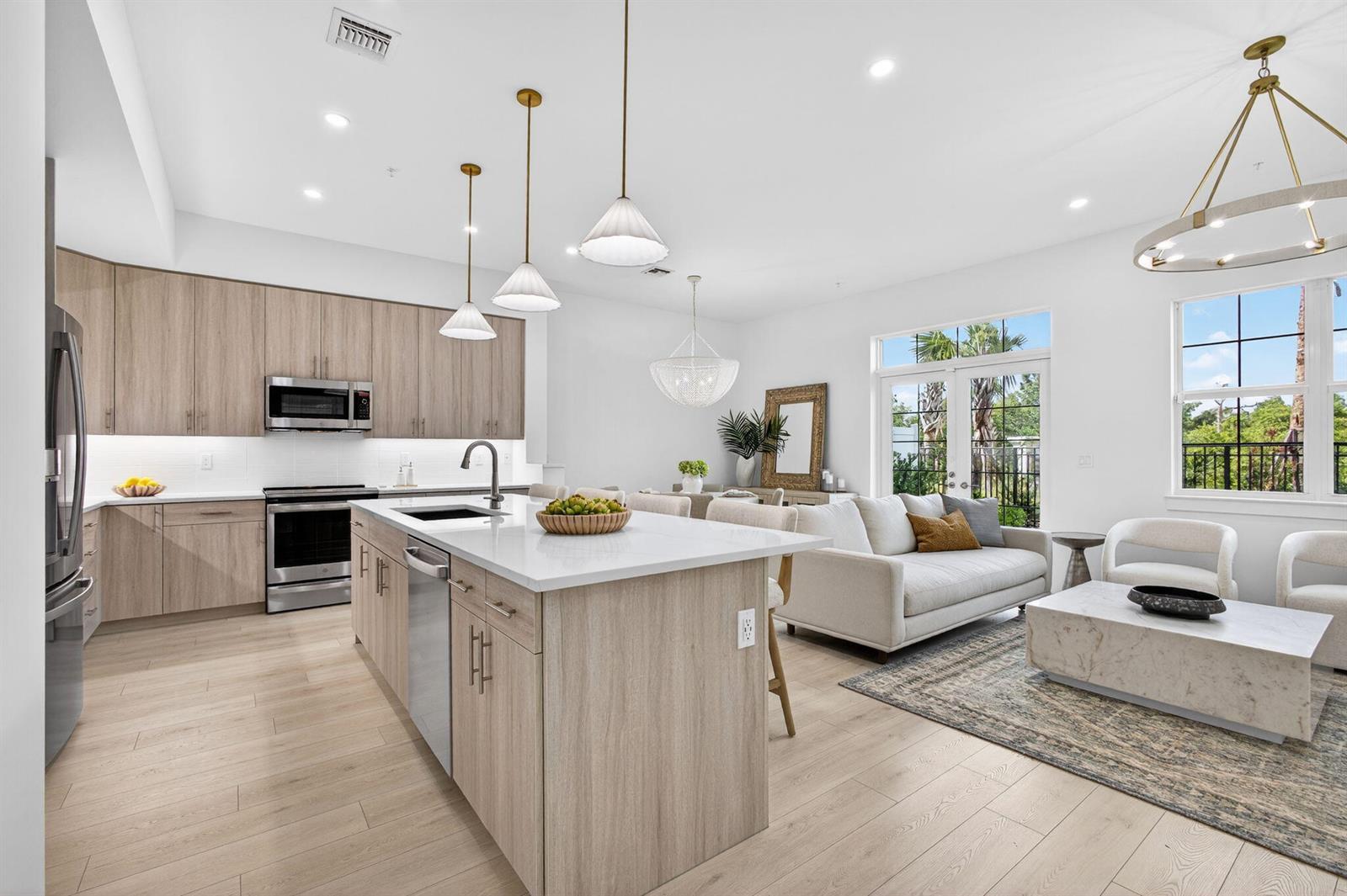 An open-concept kitchen and living area features light wood cabinetry, white countertops, and modern lighting — 125 Water Pointe Place # 26, Jupiter FL 33477, JUPITER, FL