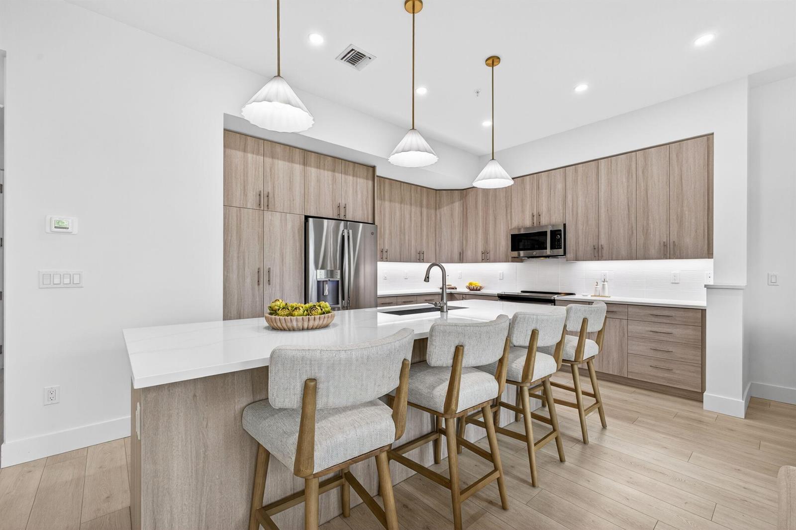 A modern kitchen features light wood cabinets, a white quartz island, and four upholstered barstools — 125 Water Pointe Place # 26, Jupiter FL 33477, JUPITER, FL