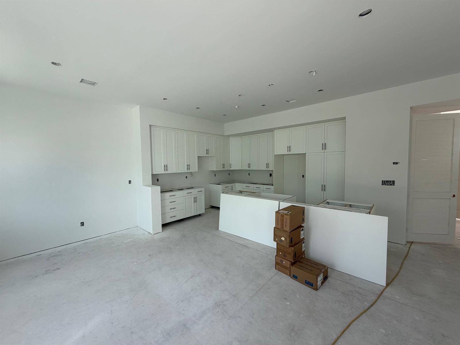 An unfinished kitchen features white cabinets, a central island, and bare concrete flooring — 125 Water Pointe Place # 26, Jupiter FL 33477, JUPITER, FL