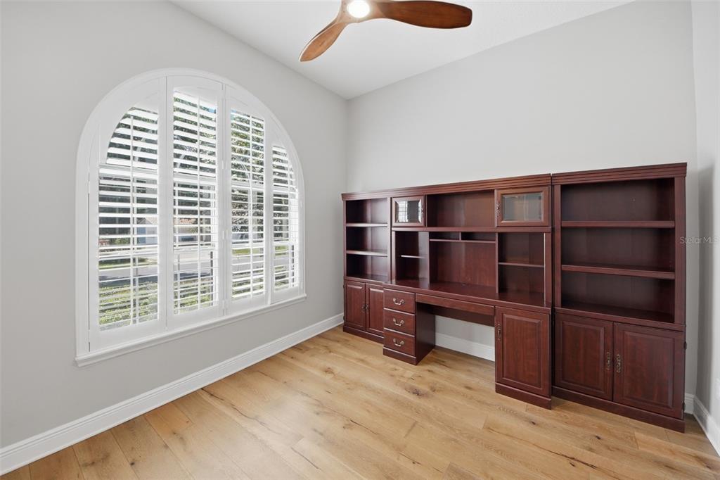 A home office features a large arched window with shutters, wood flooring, and built-in cabinetry — 5741 BAY SIDE DRIVE, ORLANDO, FL
