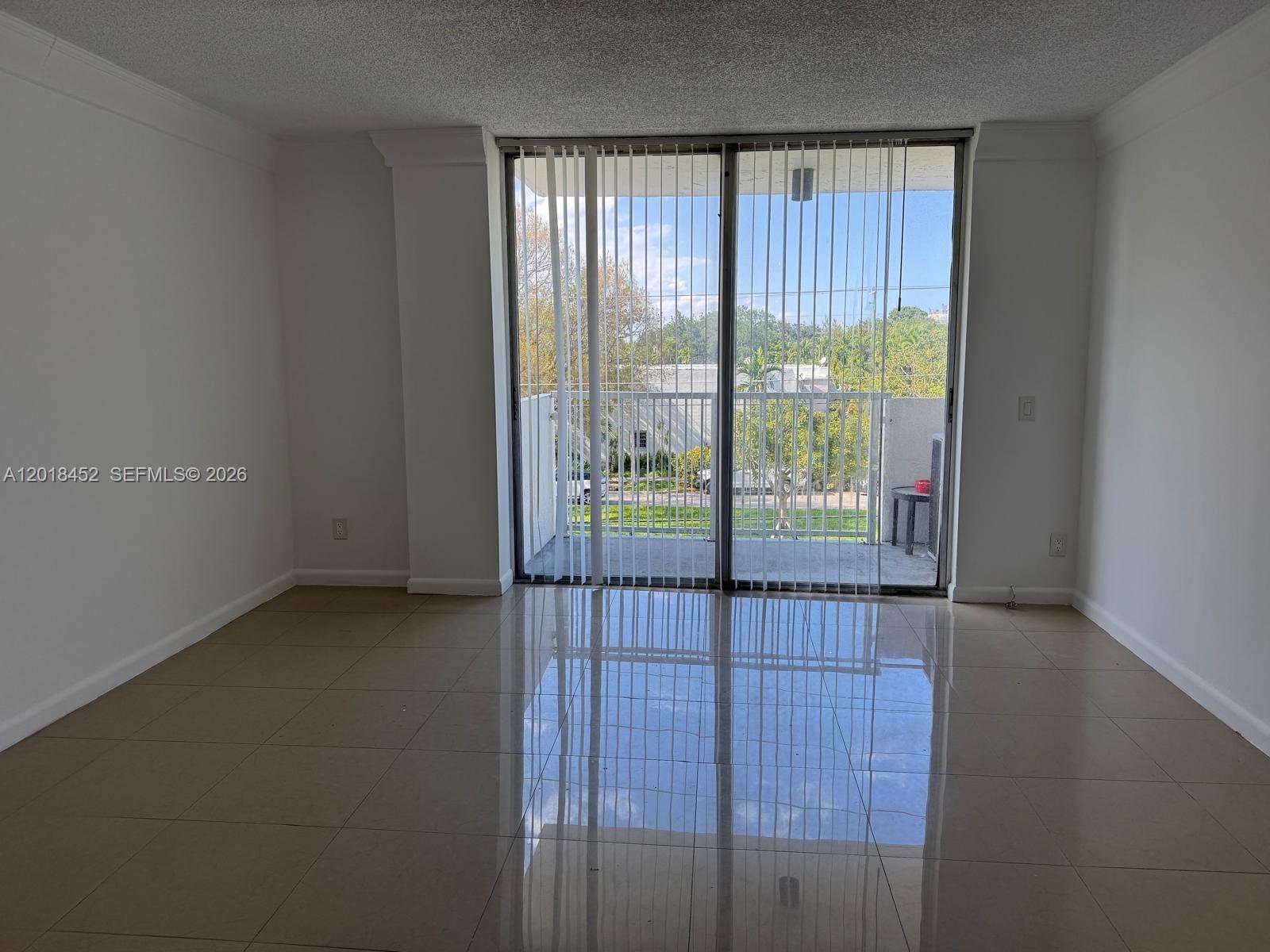 An empty room features beige tile flooring, white walls, and a sliding glass door — 2020 NE 135th St # 303, North Miami FL 33181, NORTH MIAMI, FL