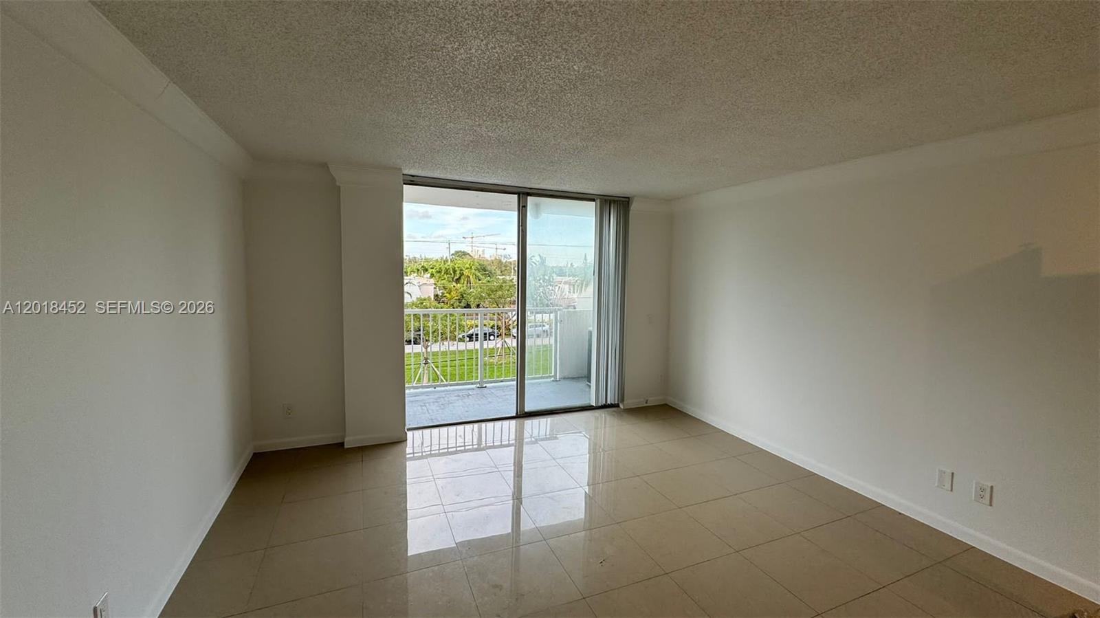 An empty room features beige tile flooring, white walls, and a sliding glass balcony door — 2020 NE 135th St # 303, North Miami FL 33181, NORTH MIAMI, FL