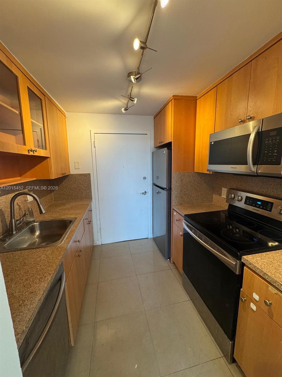A galley kitchen features light wood cabinets, granite countertops, and stainless steel appliances — 2020 NE 135th St # 303, North Miami FL 33181, NORTH MIAMI, FL
