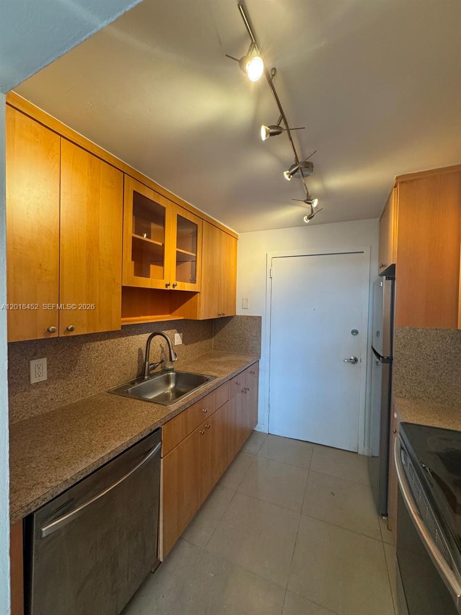 A galley kitchen features wood cabinets, granite countertops, stainless steel appliances, and track lighting — 2020 NE 135th St # 303, North Miami FL 33181, NORTH MIAMI, FL