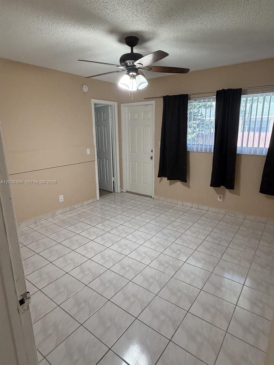 An empty room features light-colored tile flooring, beige walls, a ceiling fan, and a door — 812 NE 2nd St # 2, Hallandale Beach FL 33009, HALLANDALE BEACH, FL