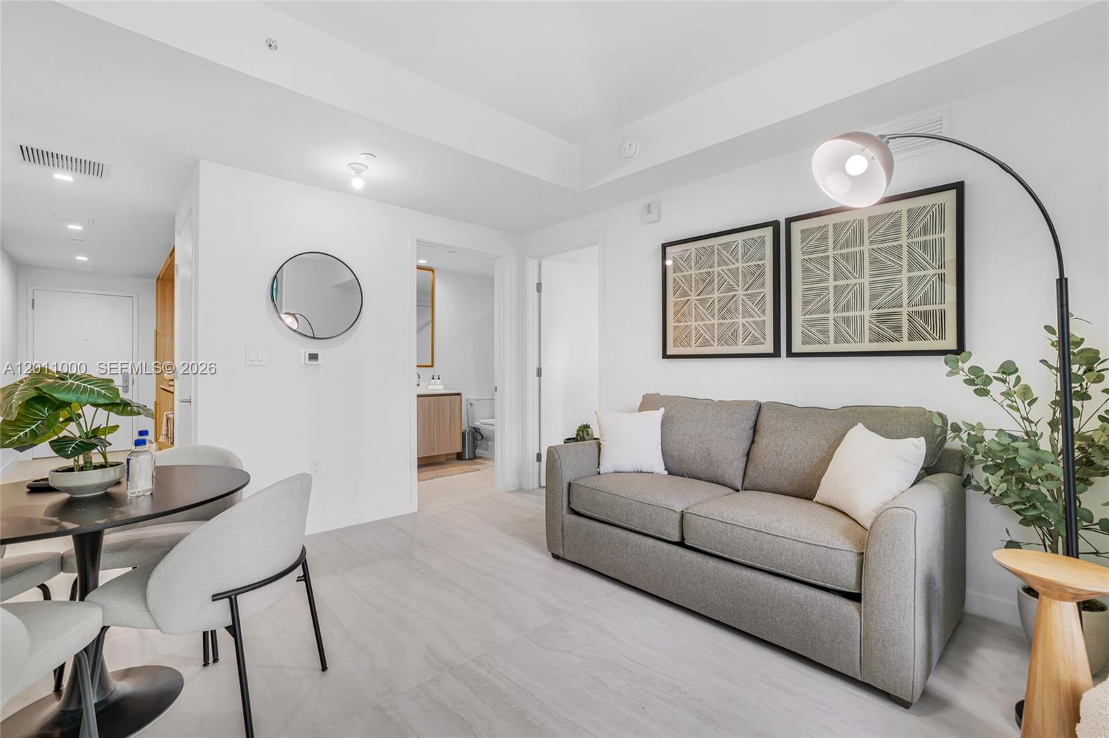 A living and dining area features a gray sofa, a round table, and light flooring — 77 SE 5TH ST # 3305, Miami FL 33131, MIAMI, FL