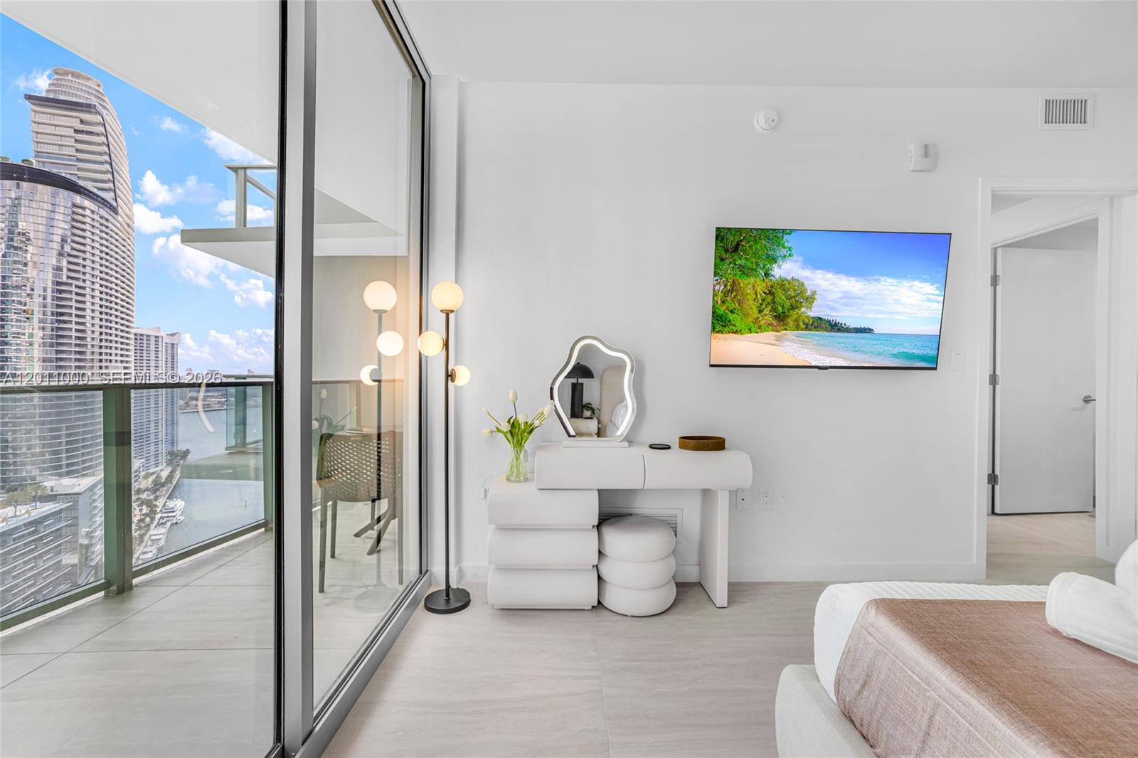 A modern bedroom features a white vanity, a wall-mounted television, and a balcony with views — 77 SE 5TH ST # 3305, Miami FL 33131, MIAMI, FL