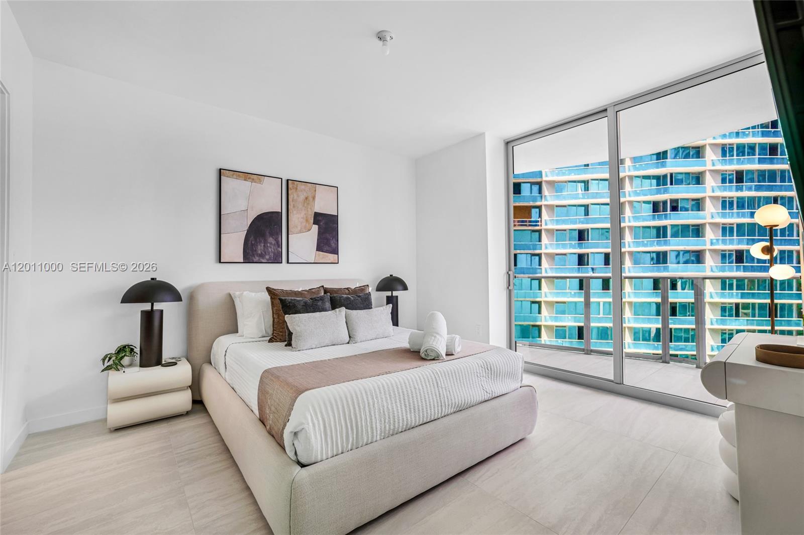A modern bedroom features a bed, two lamps, wall art, and floor-to-ceiling windows — 77 SE 5TH ST # 3305, Miami FL 33131, MIAMI, FL