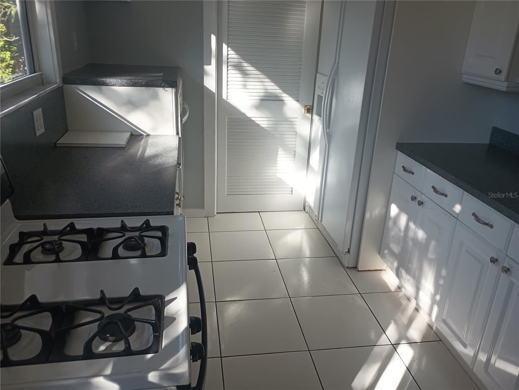 A kitchen features white cabinets, dark countertops, a gas stove, and white tile flooring — 774 32ND AVENUE N, ST PETERSBURG, FL