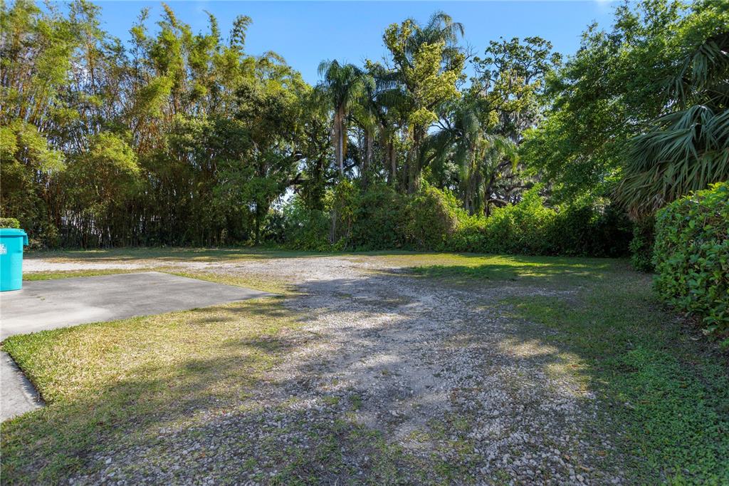 A gravel and concrete driveway leads toward a dense line of trees and foliage — 827 IRMA AVENUE, ORLANDO, FL