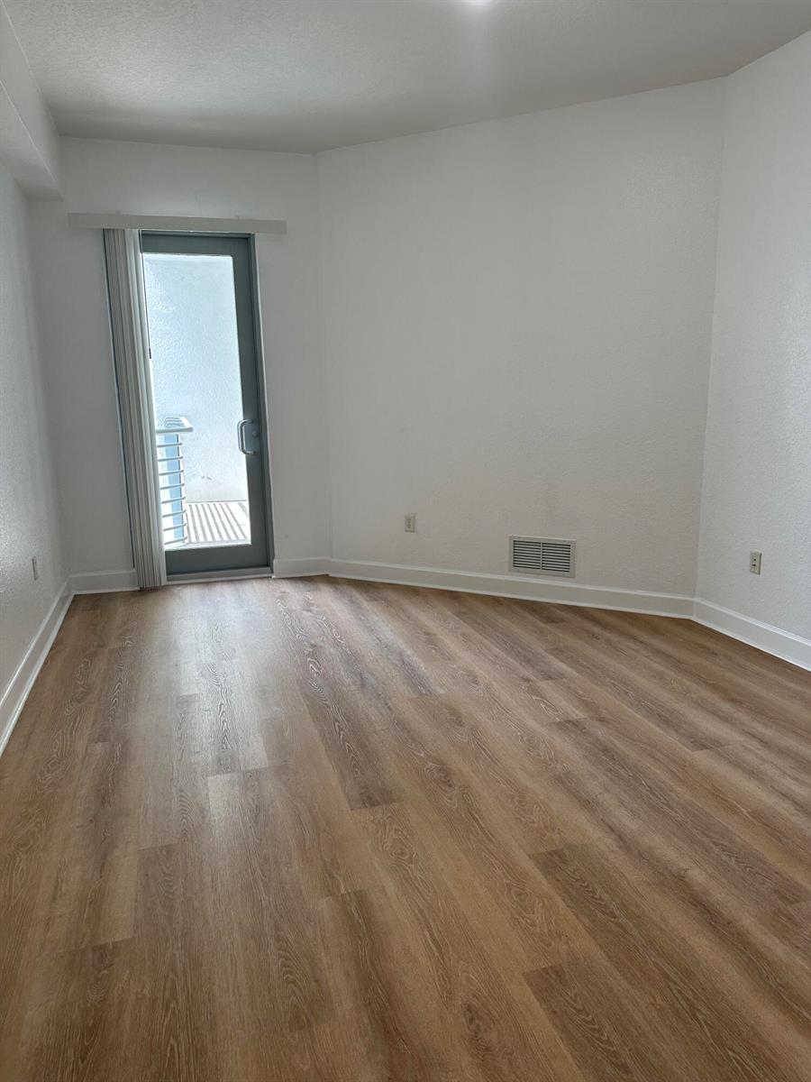 An empty room with light wood-look flooring, white walls, and a glass door to a balcony — 1830 Radius Drive # 1220, Hollywood FL 33020, HOLLYWOOD, FL
