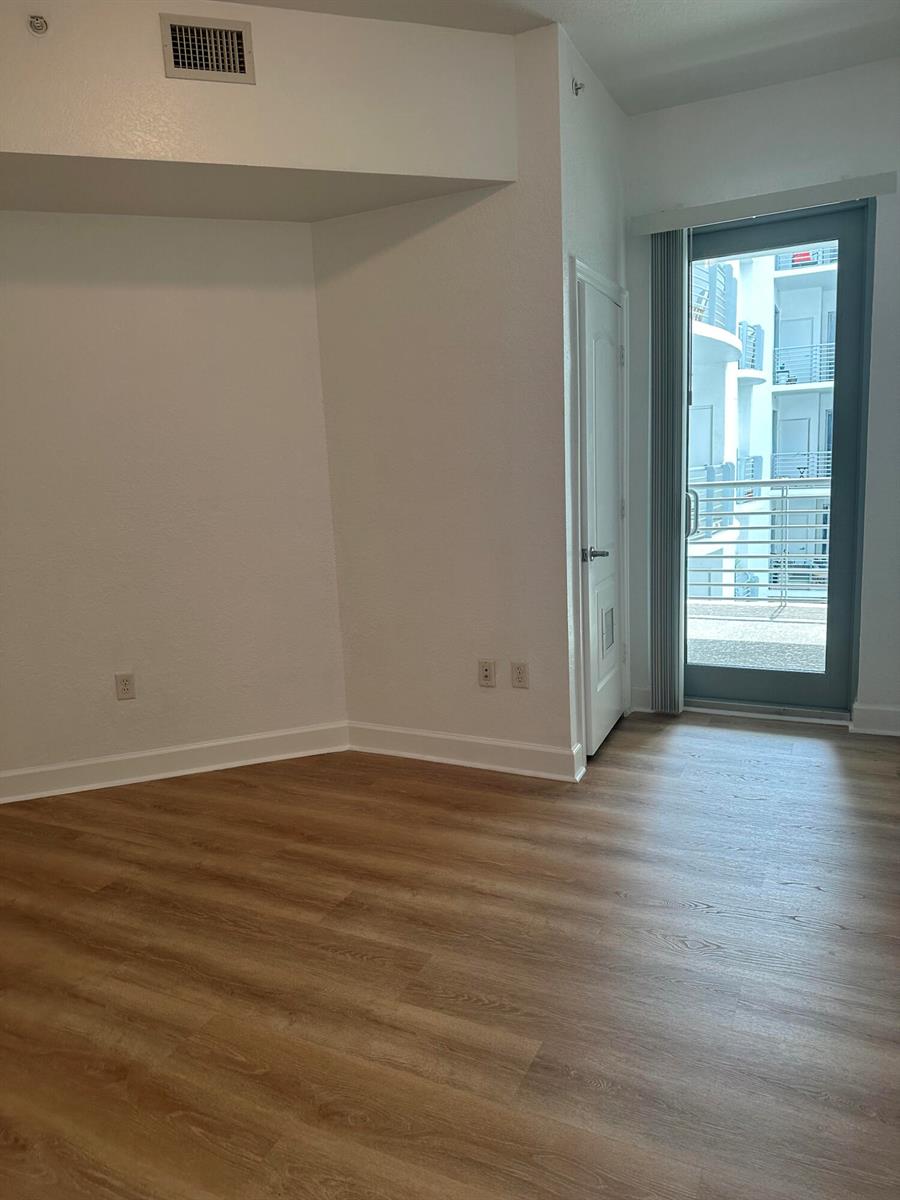 An empty room with light wood-look flooring, a white door, and a glass balcony door — 1830 Radius Drive # 1220, Hollywood FL 33020, HOLLYWOOD, FL