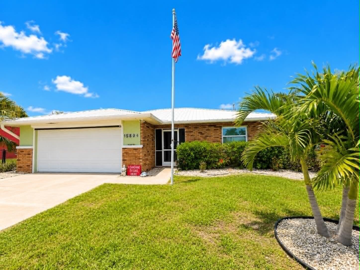A single-story brick house with a white garage door, metal roof, and American flag pole — 15804 Missouri Street, FL 33922, FL