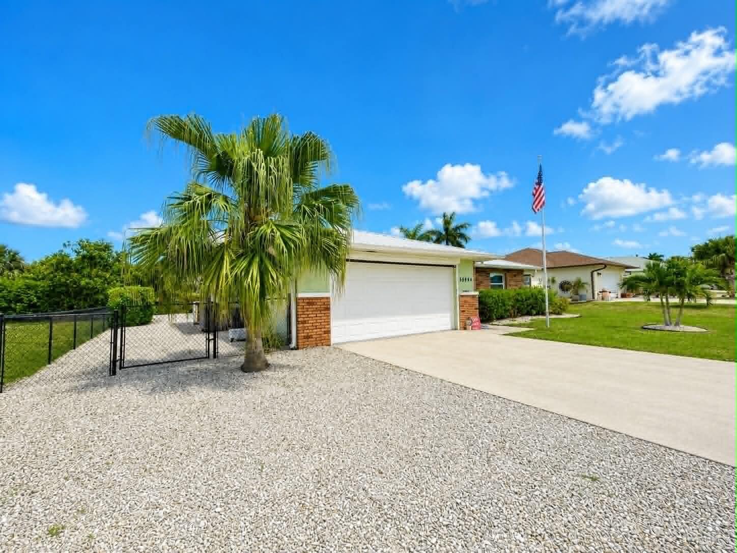 A single-story house with a white garage door, gravel yard, and a palm tree — 15804 Missouri Street, FL 33922, FL