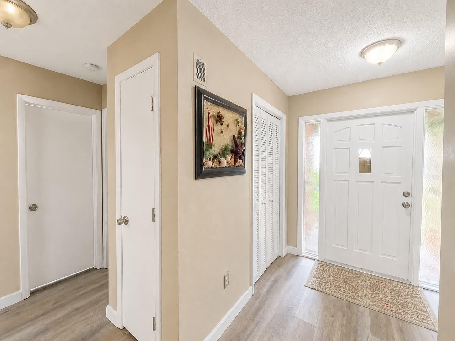 An entryway features light-colored walls, wood-look flooring, white doors, and a decorative wall art piece — 15804 Missouri Street, FL 33922, FL