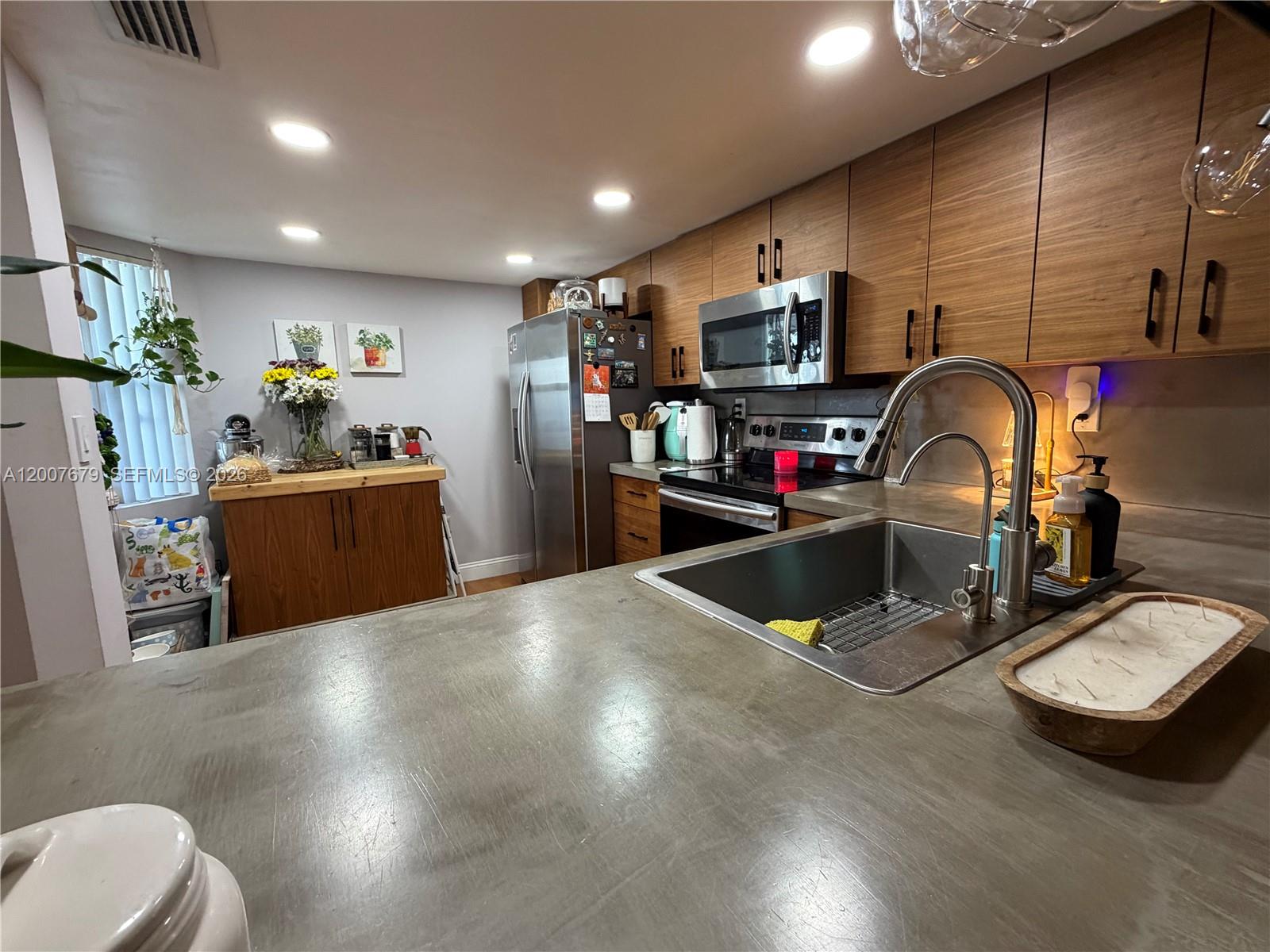 A kitchen features concrete countertops, wood-toned cabinets, stainless steel appliances, and a stainless steel sink — PEMBROKE PINES, FL
