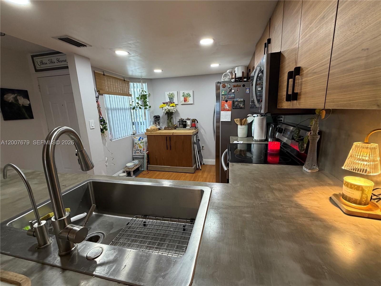 A kitchen features a stainless steel sink, concrete countertops, and wood-toned upper cabinets — PEMBROKE PINES, FL