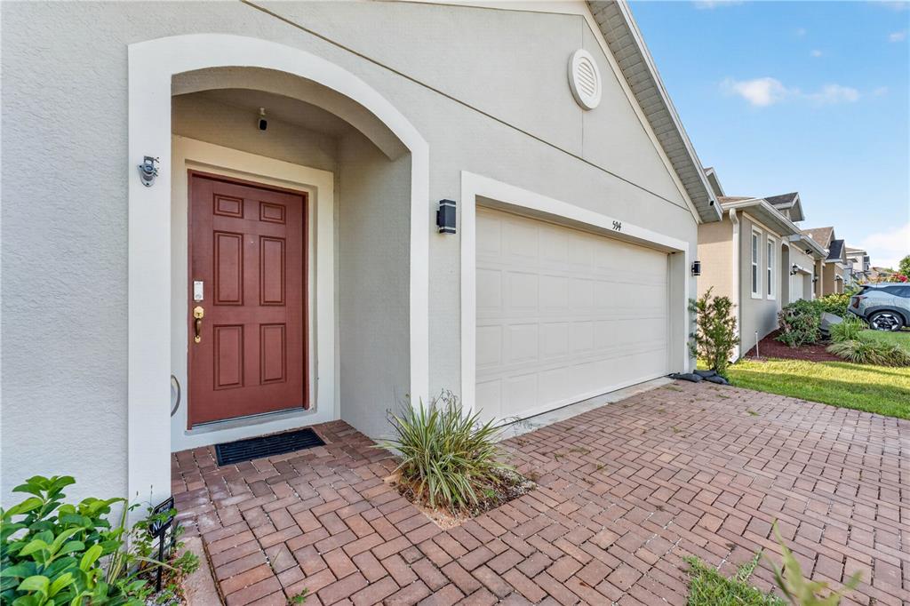 The exterior of a house features a red front door, a garage, and a brick driveway — 594 BELLINGHAM WAY, MINNEOLA, FL