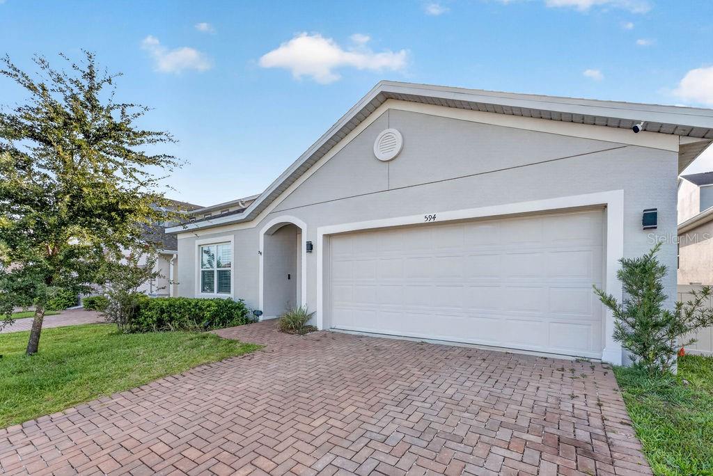 A single-story house with a light gray exterior, a two-car garage, and a brick driveway — 594 BELLINGHAM WAY, MINNEOLA, FL