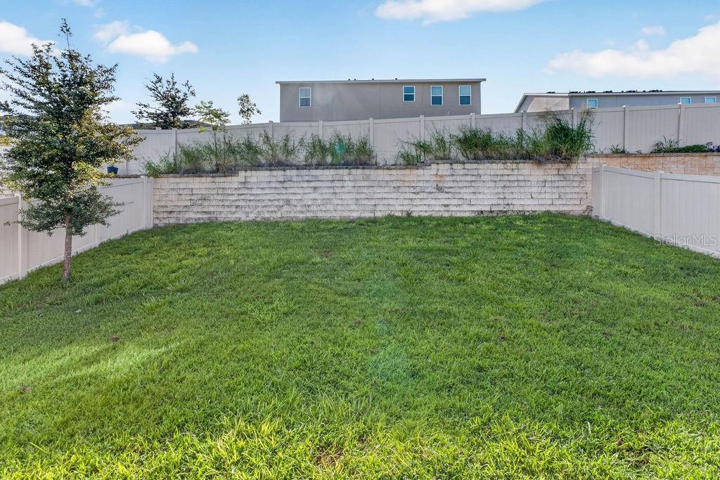 A grassy backyard features a retaining wall and a white vinyl privacy fence — 594 BELLINGHAM WAY, MINNEOLA, FL