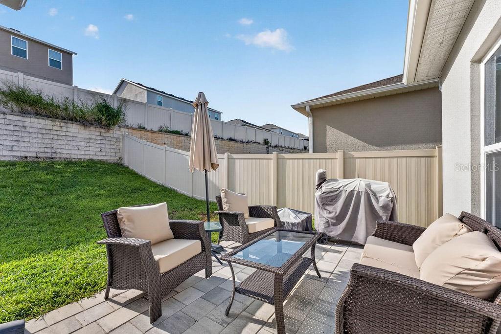A patio with wicker furniture and a grill sits in a fenced backyard — 594 BELLINGHAM WAY, MINNEOLA, FL